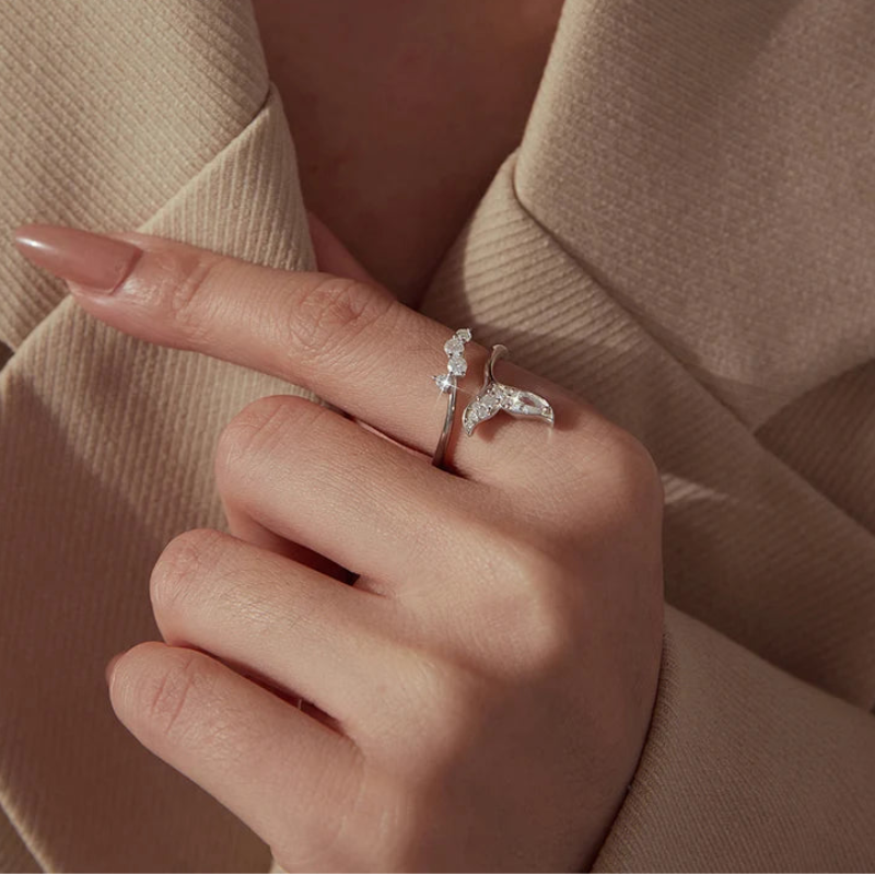 A close-up of a hand wearing a silver branch-shaped ring with clear stones, styled with a beige blazer.