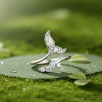 A sterling silver mermaid tail ring with clear cubic zirconia stones, displayed on a textured rock with a soft green background.