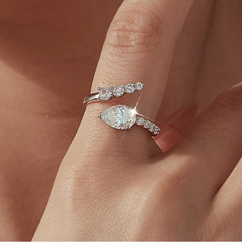 A close-up of a hand wearing a silver-tone ring with a marquise-cut clear gemstone and smaller clear stones along the band, with a second matching ring shown beside it.