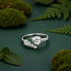 A sterling silver open ring ring with a leaf-like top and a teardrop-shaped clear gemstone, resting on a textured stone with green moss in the foreground.