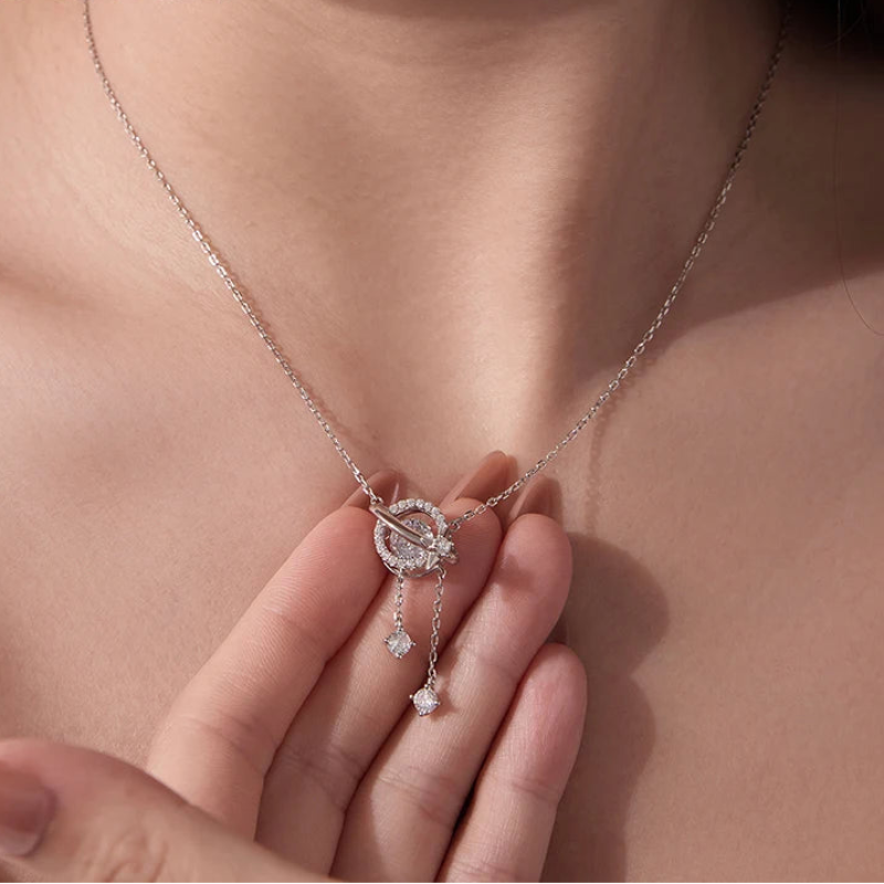 A close-up of a model wearing a delicate silver chain necklace with a celestial moon and star pendant. The pendant is adorned with small clear stones and features two dangling star charms.