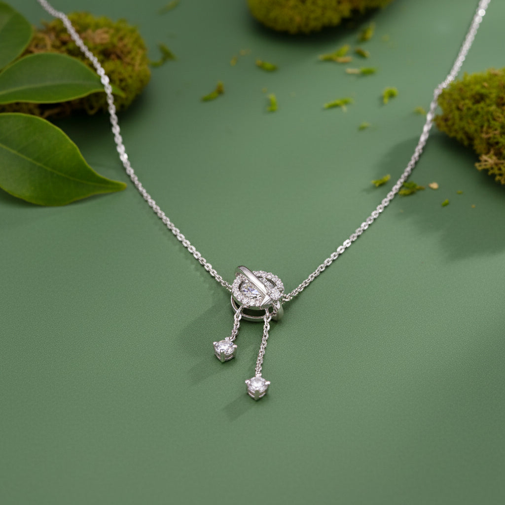 A sterling silver pendant necklace with a circular ring design and dangling clear stones, displayed against a sage green background.