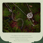 A silver-toned chain necklace with a round clear stone pendant and small dangling beads, laid on dark mossy ground. The photo is framed by a pale green border with disclaimer text below.