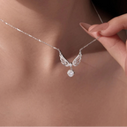 A close-up lifestyle shot of a model wearing a silver angel wing pendant necklace with a clear faceted gemstone, with a hand gently holding the chain.