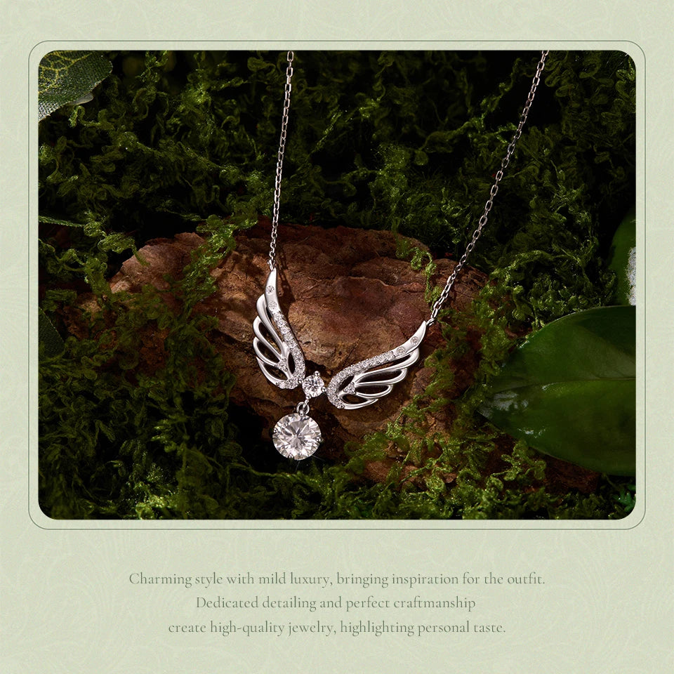 A silver-toned angel wing pendant necklace with a clear round gemstone, displayed on a mossy brown log with green leaves. The photo is framed with a light green border containing descriptive text at the bottom.