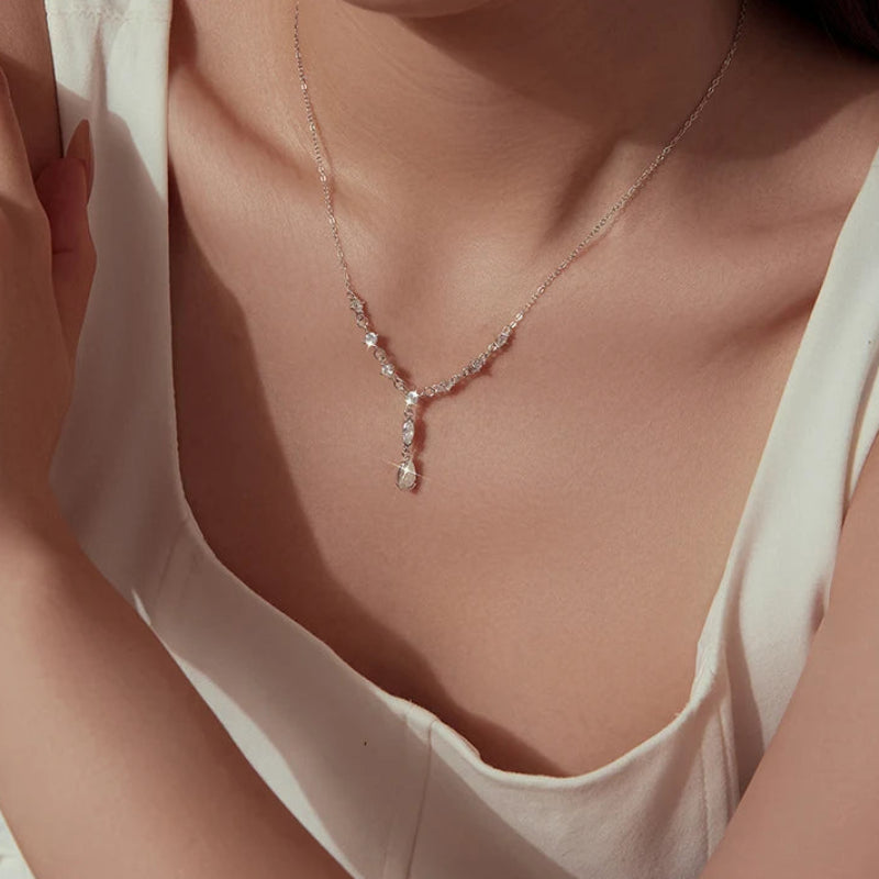 A close-up lifestyle shot of a model wearing a delicate silver Y-shaped necklace adorned with clear crystals, paired with a cream-colored top.