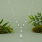 A silver Y-shaped necklace featuring a delicate chain, star-shaped links, and a teardrop pendant, all adorned with clear sparkling stones, set against a plain sage green background.