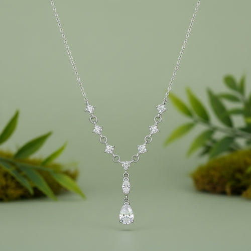 A silver Y-shaped necklace featuring a delicate chain, star-shaped links, and a teardrop pendant, all adorned with clear sparkling stones, set against a plain sage green background.