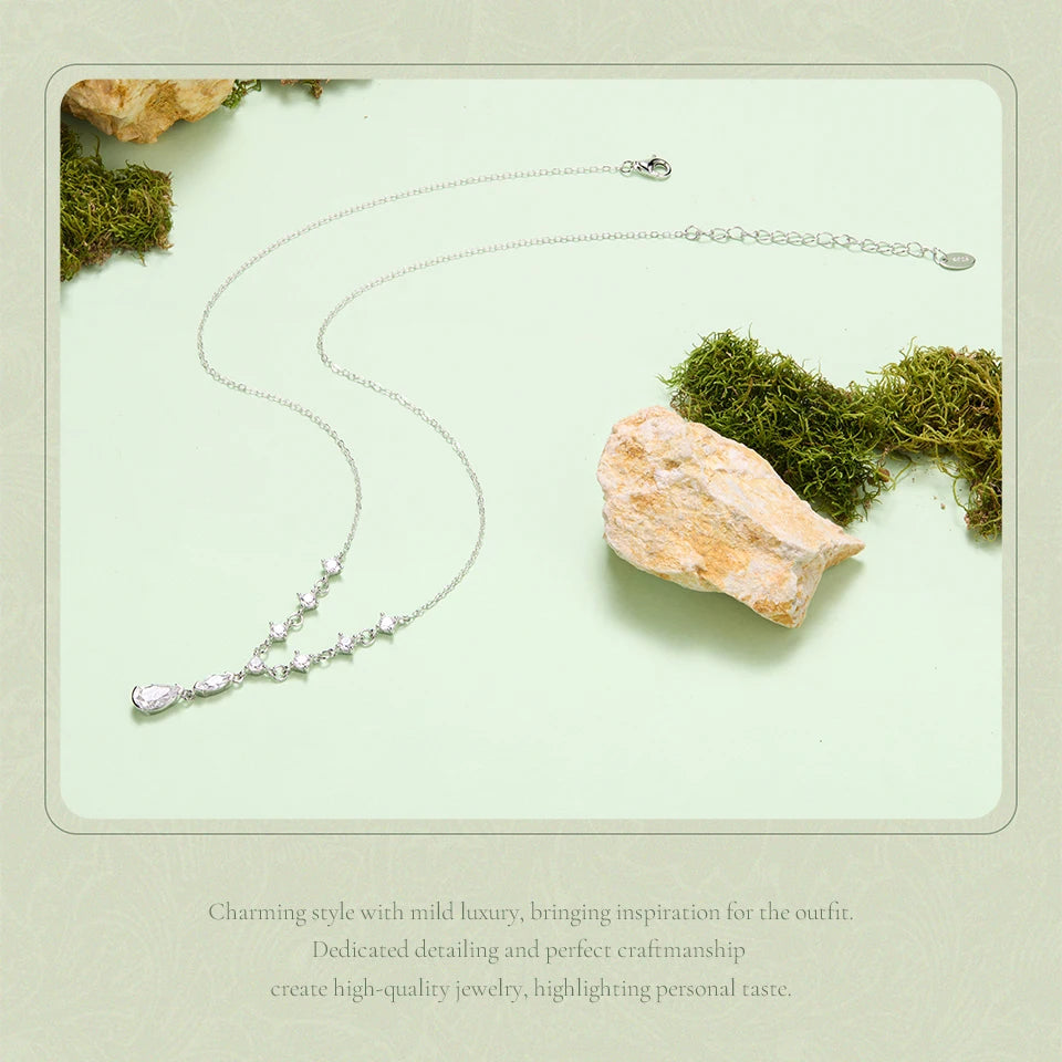 A delicate silver necklace with a small cluster of clear stones at the center, displayed on a pale mint green background with decorative moss and a stone. Chinese promotional text is printed at the bottom.