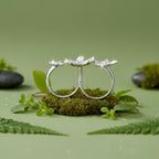 Sterling silver three-flower ring set with clear gemstones, displayed on a mint green background.