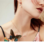Close-up of a woman wearing a butterfly necklace and earrings with a neutral background