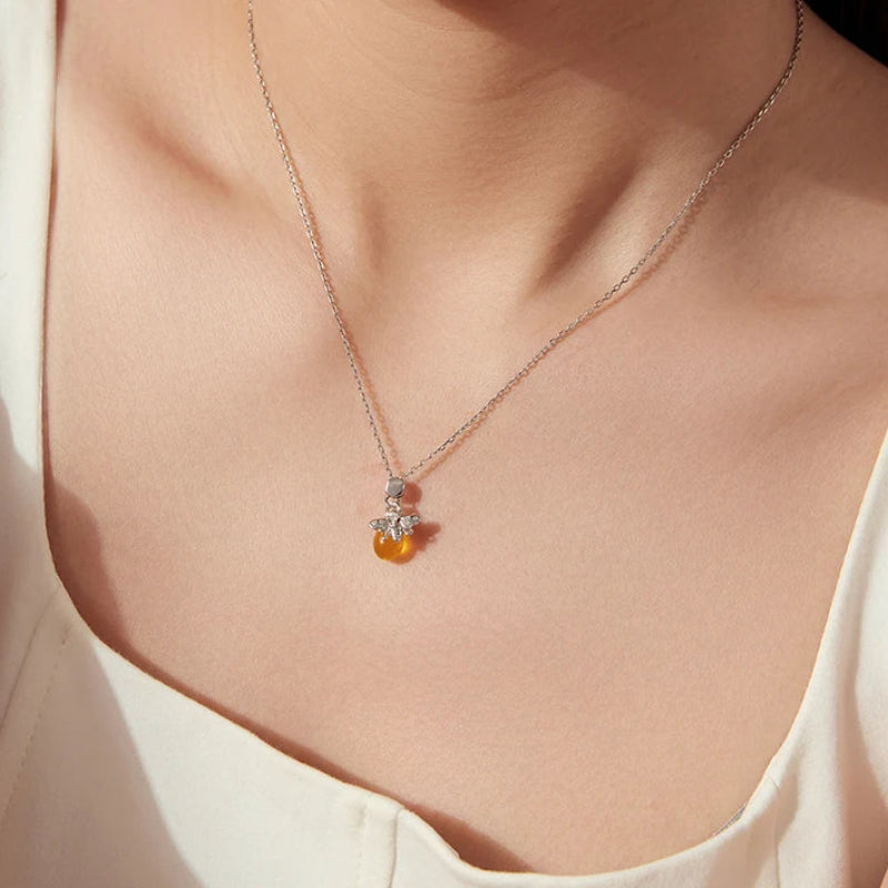 A close-up of a model wearing a delicate silver chain necklace with a small pendant featuring a clear crystal and a yellow amber bead.
