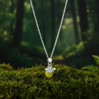 A silver-tone chain necklace with a small bee charm holding a translucent yellow-green bead, displayed on a light blue cylindrical stand.