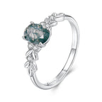 Silver ring with a green gemstone and leaf designs on a white background.