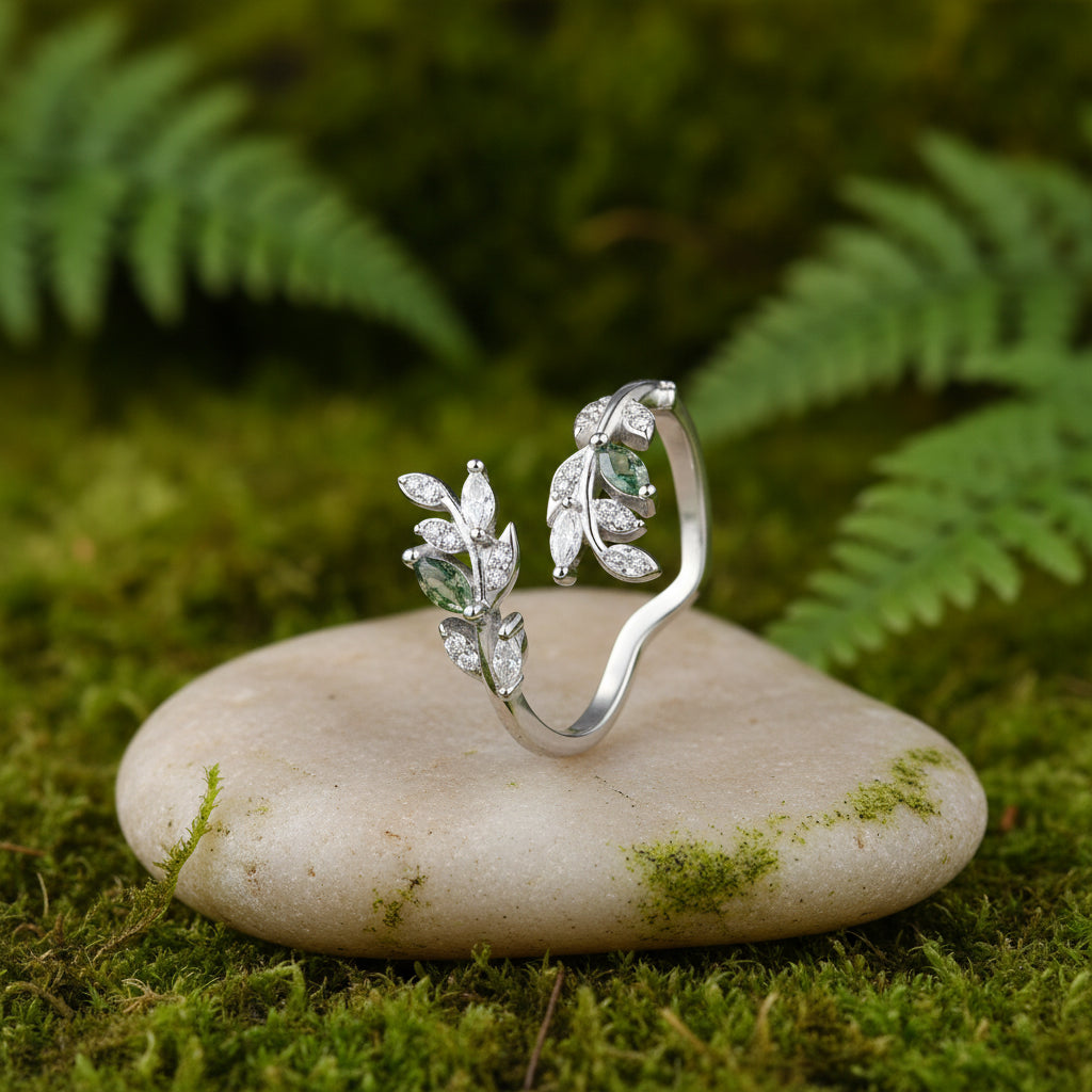 A silver-toned ring with leaf-shaped crystal clusters and a small grey stone, displayed on a piece of stone against a soft green background.