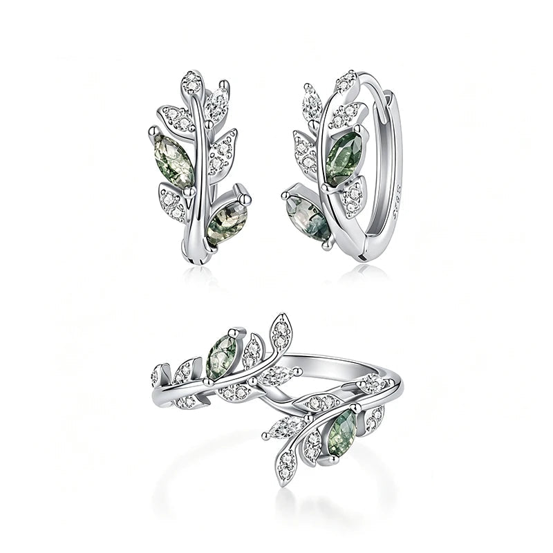 A jewelry set featuring a silver huggie hoop earring, a matching leaf-shaped ring, all adorned with green marquise-cut gemstones and clear pavé crystals on a white background.