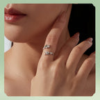 A close-up of a model's hand and lower face wearing two delicate silver rings with small clear stones and leaf-like details, set against a soft light green background.