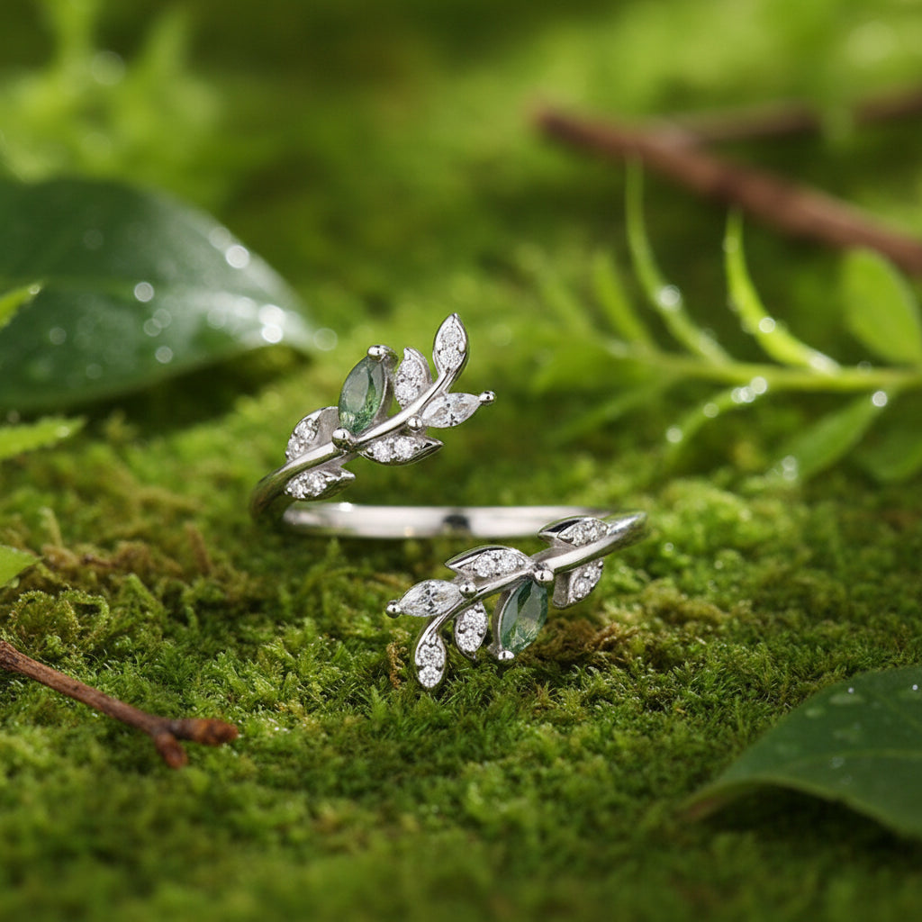 A sterling silver leaf-shaped ring with clear cubic zirconia stones and light blue-green oval gemstones, displayed on grass and a soft grass green background.