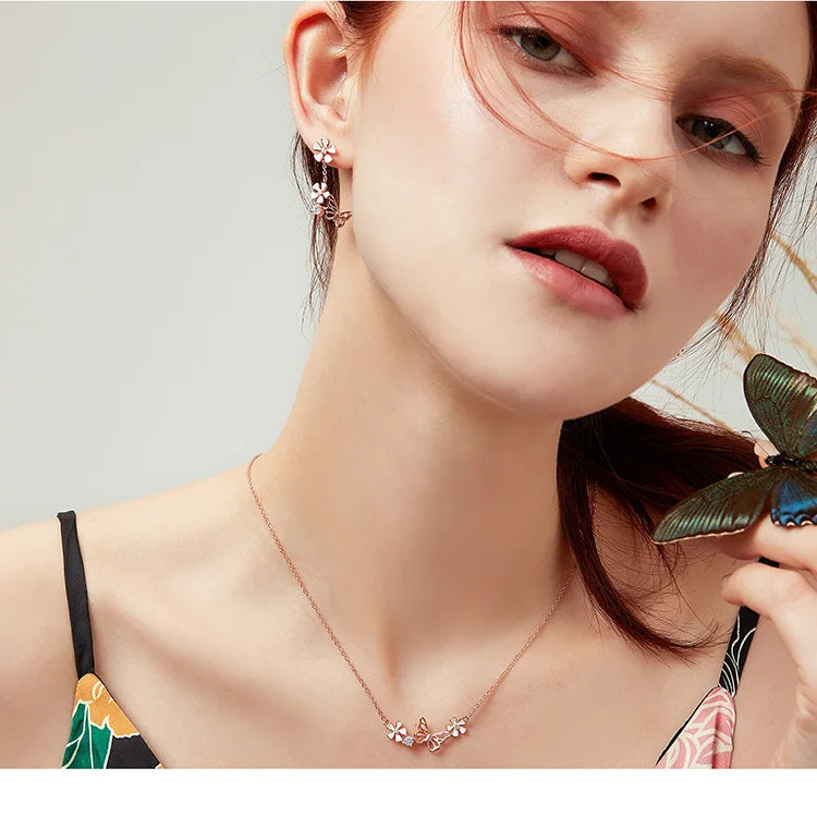 Woman wearing a butterfly-themed necklace and earrings with a butterfly in the background