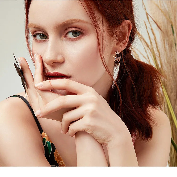 Woman with red hair wearing earrings and a black top, with a blurred natural background